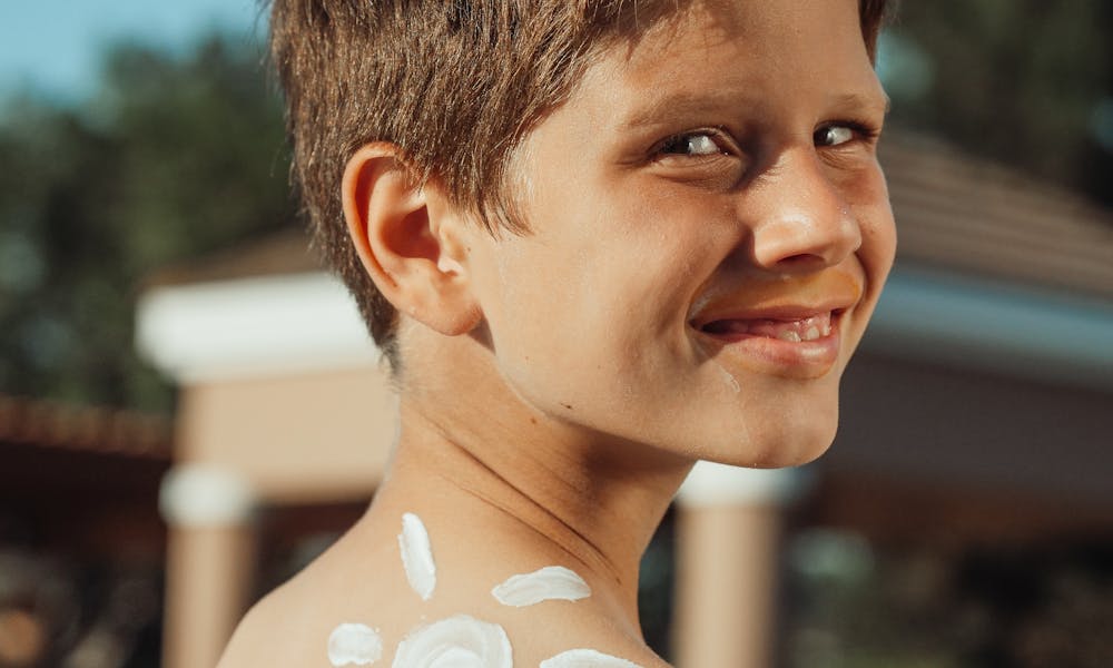 Smiling boy with sunscreen arranged in a sun shape on his back, outdoors. .pexels