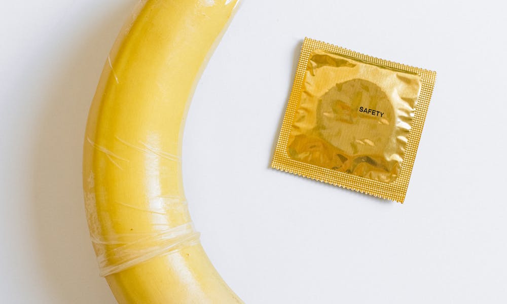 A banana wrapped in a condom next to a packaged condom on a white background, symbolizing safe sex education. .pexels