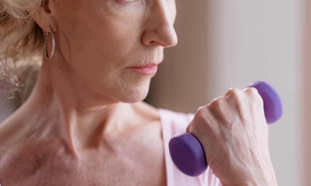 Elderly woman focused on fitness, lifting a dumbbell indoors, promoting healthy aging. .pexels