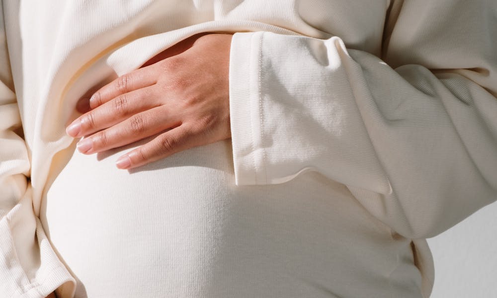 A serene close-up of a pregnant woman cradling her belly, bathed in warm sunlight. .pexels