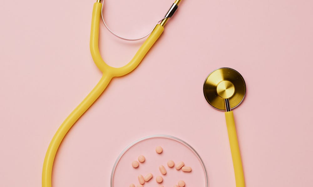 Flat lay of yellow stethoscope with pink pills on a pastel pink background. .pexels