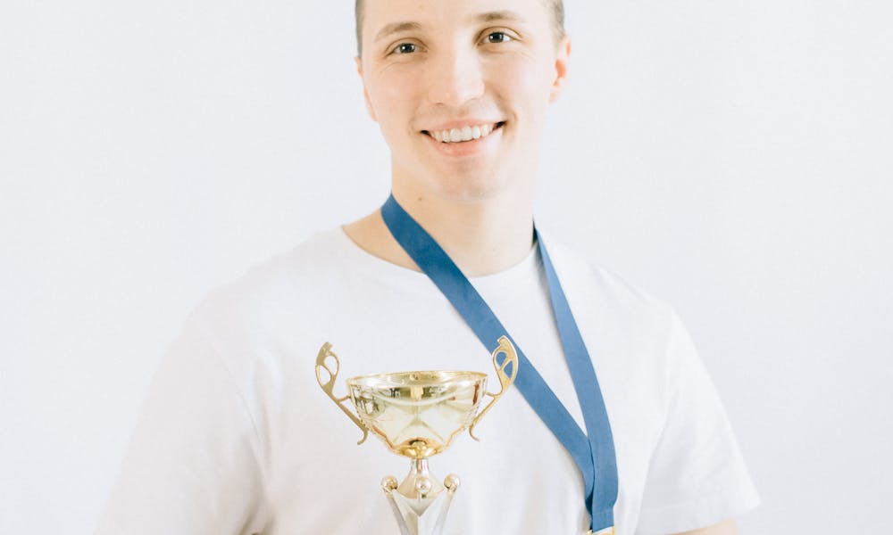 Smiling young man holding a trophy and wearing a medal, embodying success and achievement. .pexels