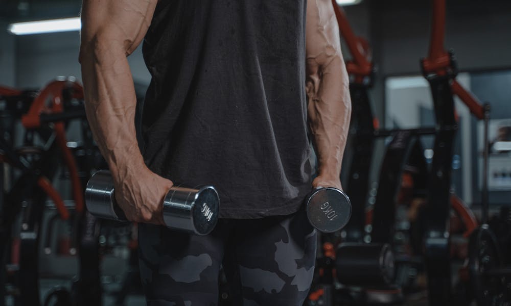 A muscular man exercising with dumbbells in a gym, showcasing strength and dedication. .pexels