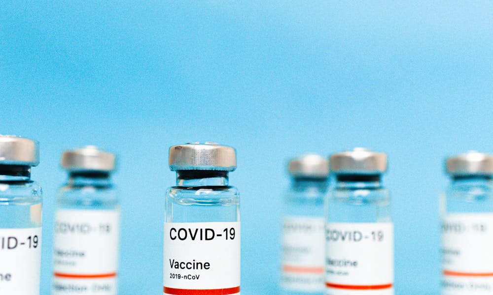 Multiple vials of COVID-19 vaccine arranged on a blue background. .pexels