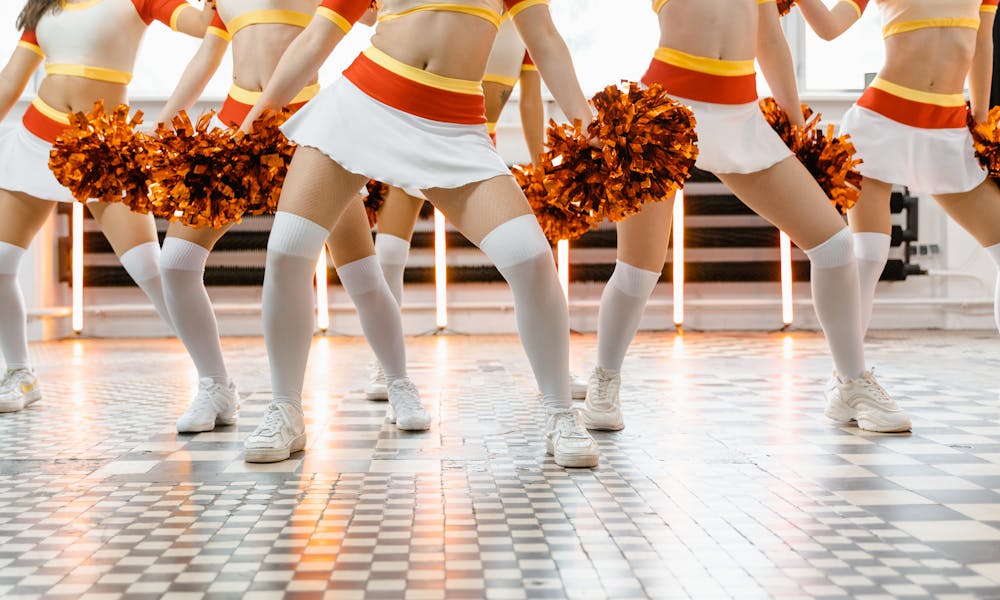 Group of cheerleaders in uniforms with pompoms dancing indoors on a patterned floor. .pexels