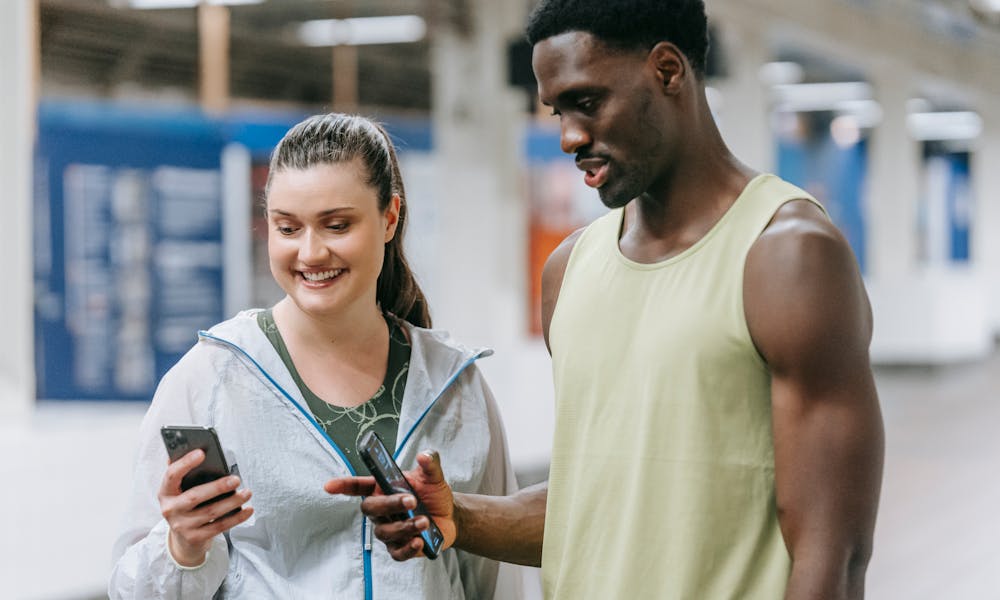 Two young adults in sports clothing sharing social media on a smartphone at a subway station. .pexels