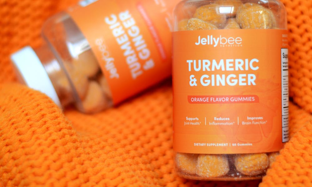 Vibrant turmeric and ginger gummies bottle displayed on textured orange fabric. .pexels