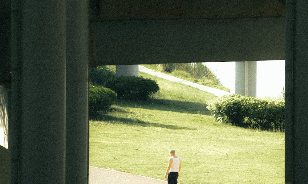 A lone jogger runs under a city overpass framed by greenery on a sunny day. .pexels