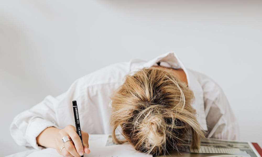 Frustrated woman overwhelmed with work, head down on desk in home office. .pexels