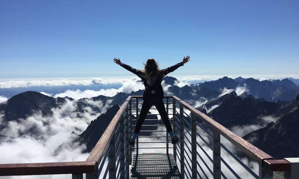 A woman stands on a viewing platform in Vysoké Tatry, Slovakia, surrounded by clouds and mountains, embracing freedom. .pexels