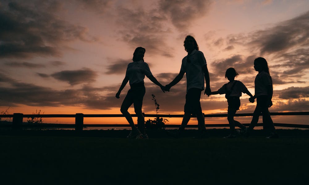 A family walks hand in hand against a vibrant sunset, evoking togetherness and peace. .pexels