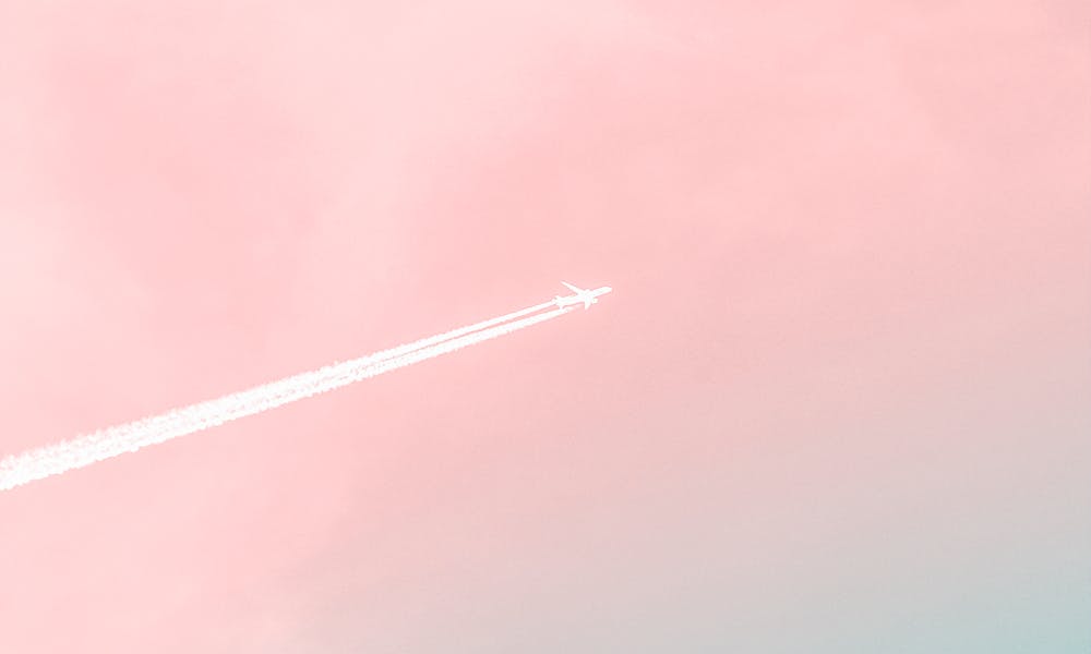 A serene view of an airplane soaring through a pastel pink and blue sky, leaving a contrail. .pexels