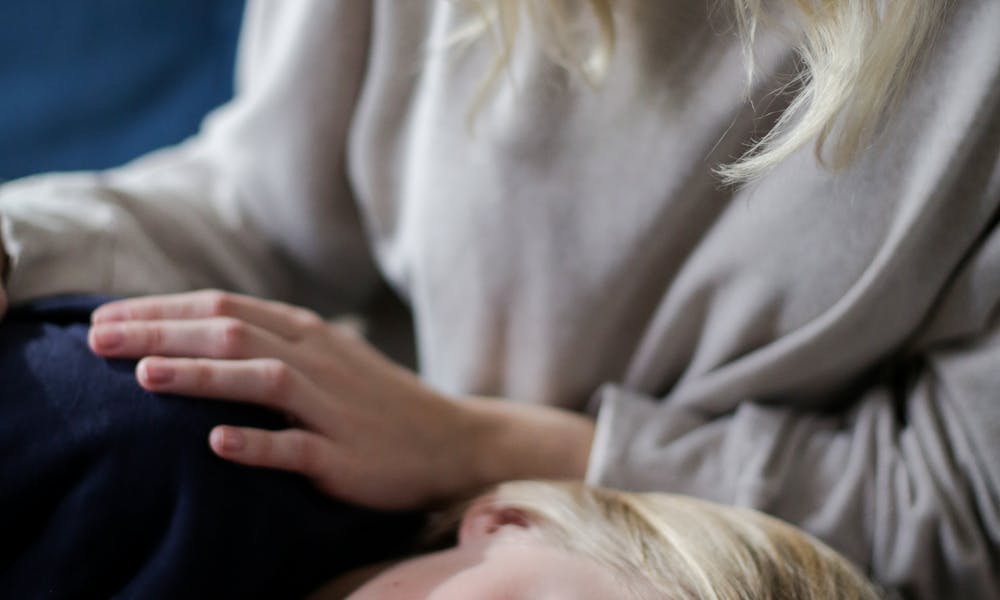 A mother comforts her sick child resting on her lap in a cozy indoor setting. .pexels