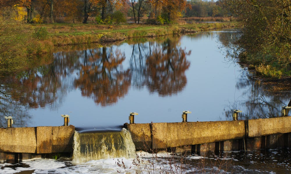 A peaceful dam and river scene in Steinhorst, Germany, surrounded by autumn trees reflecting in the water. .pexels