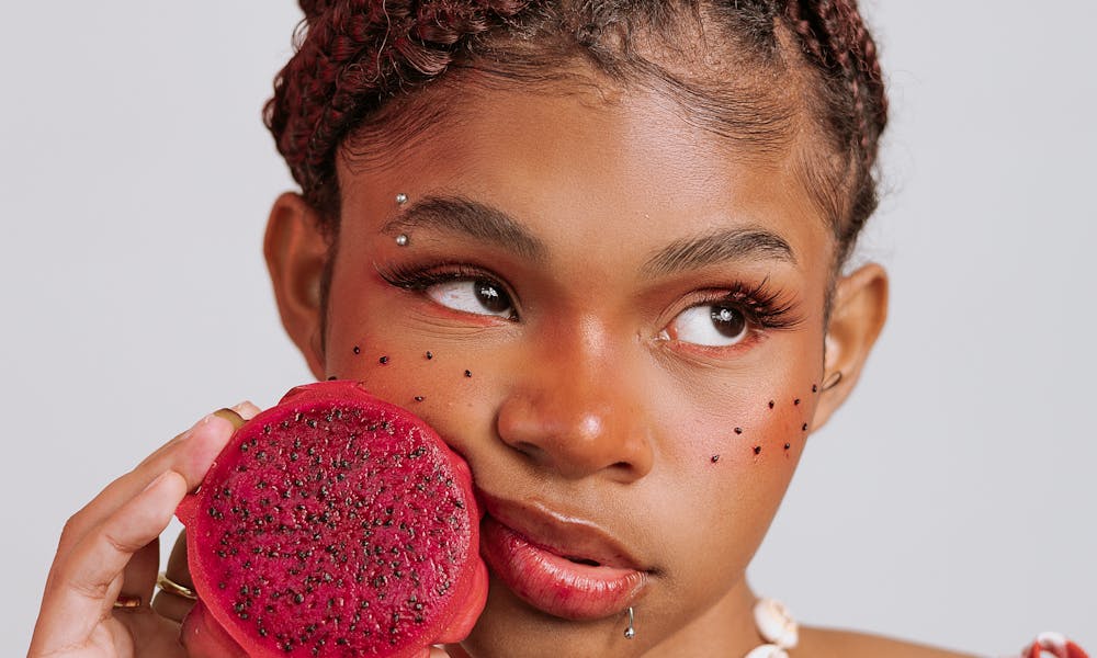 A stylish young woman with braided hair holding a vibrant dragon fruit slice. .pexels