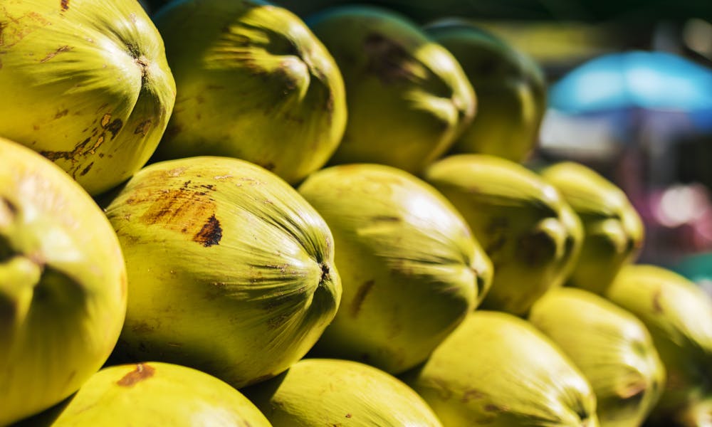 Stack of fresh green coconuts on a market stand, bathed in sunlight. .pexels