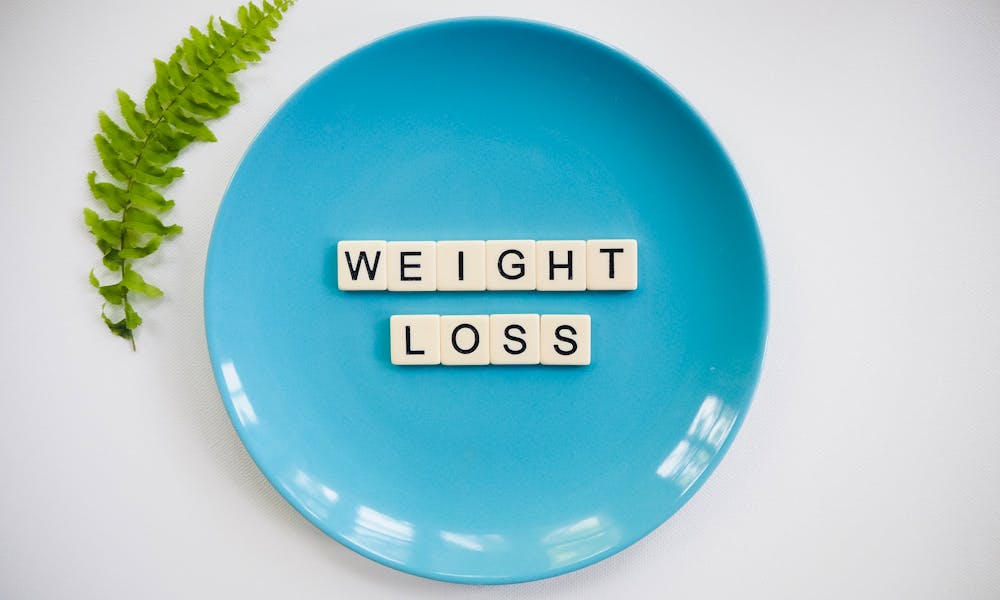 A blue plate with 'weight loss' tiles and a fern leaf on white background. .pexels