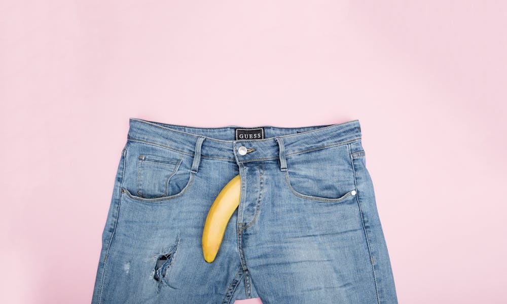 A creative still life featuring blue jeans and a banana against a pink backdrop. .pexels