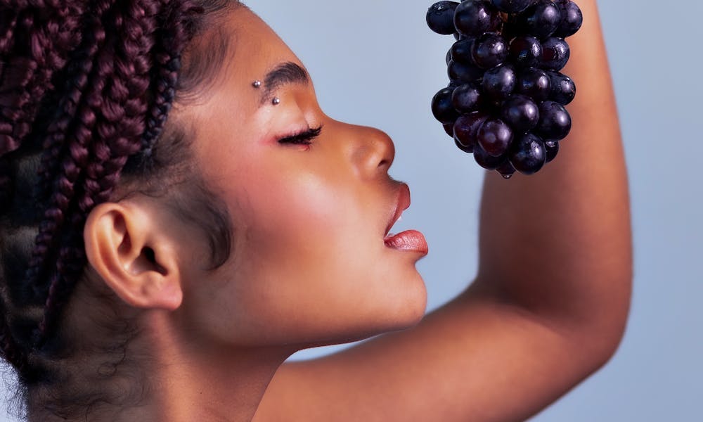 Portrait of a young woman holding a bunch of grapes with vibrant expression. .pexels