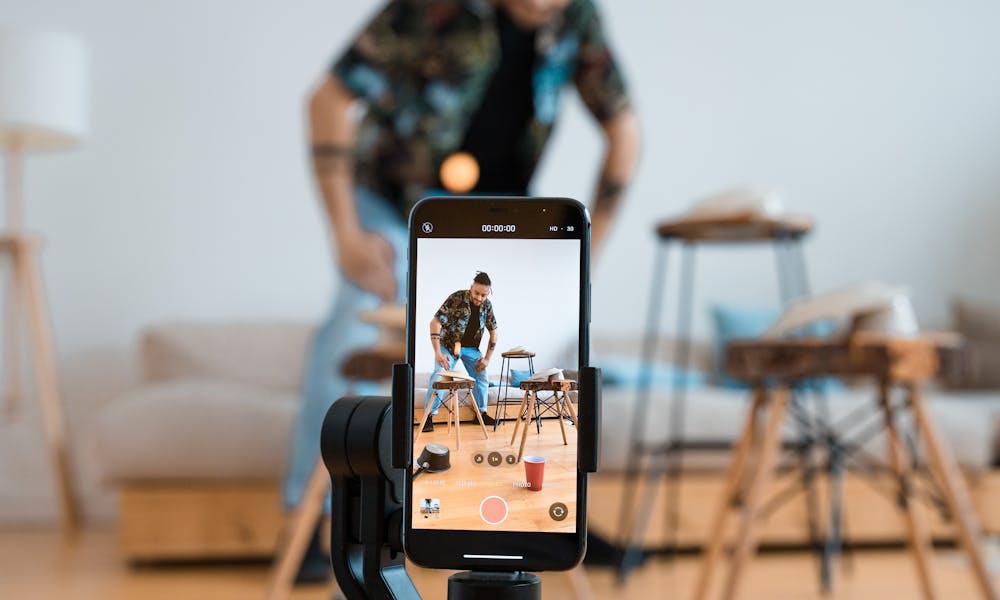 Man recording video content with smartphone on a tripod in a cozy living room. .pexels