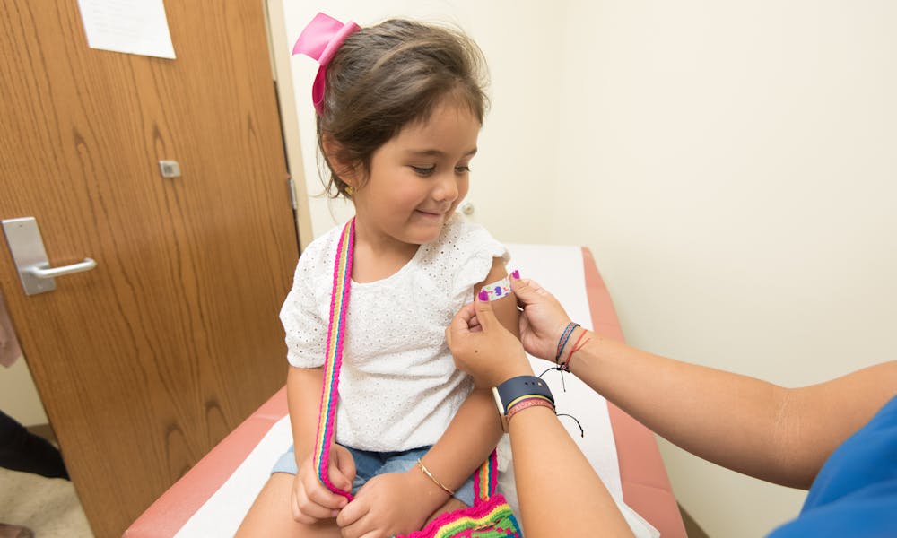 A cheerful young girl receives a band-aid after a vaccination at a clinic. .pexels