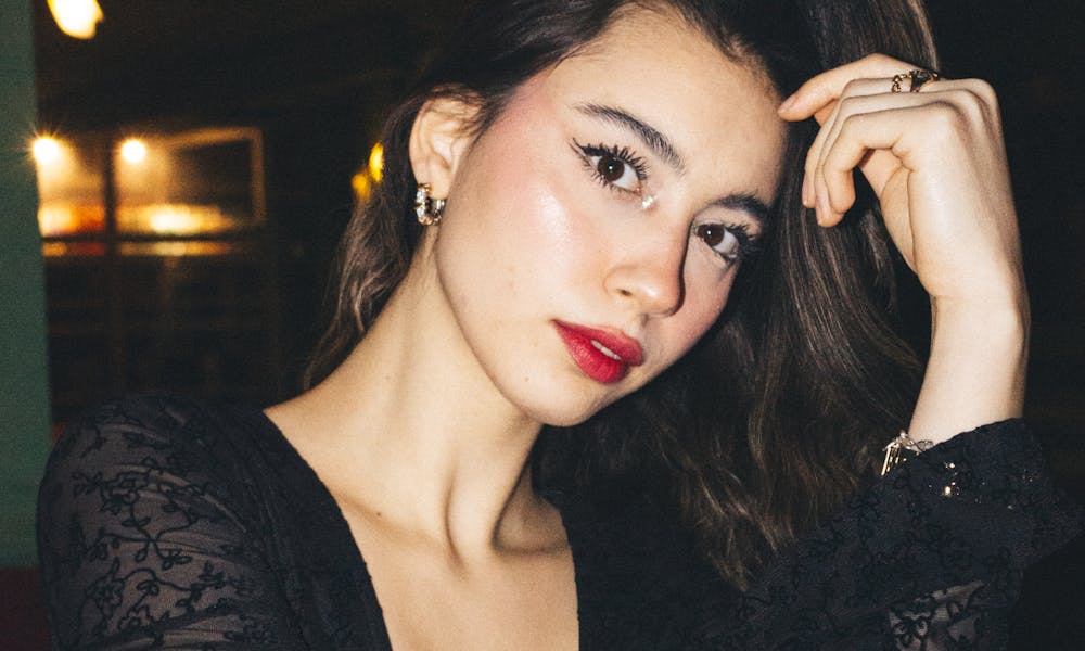 Elegant young woman in a black lace dress posing indoors with a confident expression. .pexels