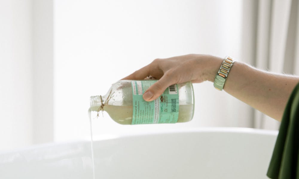 A woman pouring aromatherapy bath oil into a bathtub for a relaxing skincare routine. .pexels