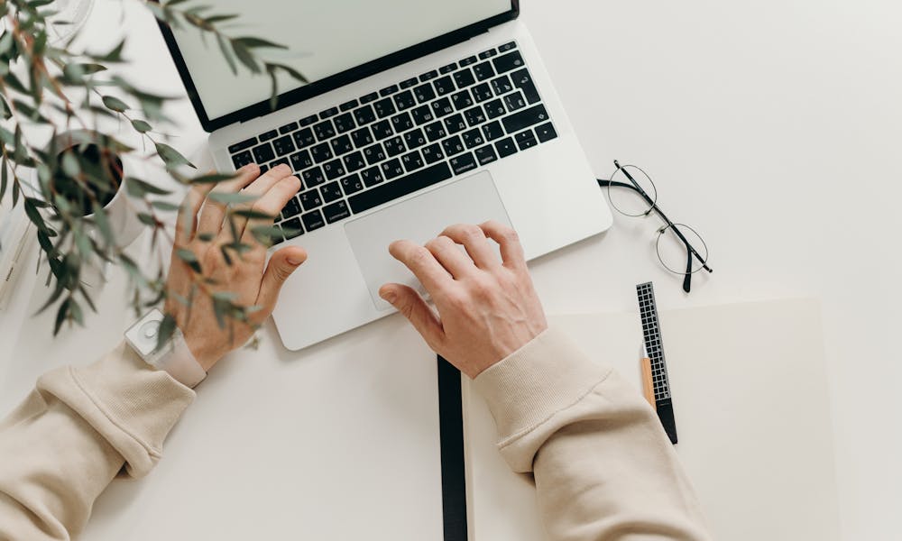 An overhead view of a person working on a laptop in a minimalist home office setting. .pexels