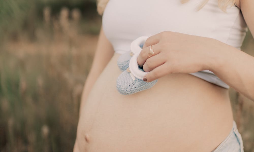 Expectant mother holds baby shoes on her belly in a serene outdoor setting. .pexels