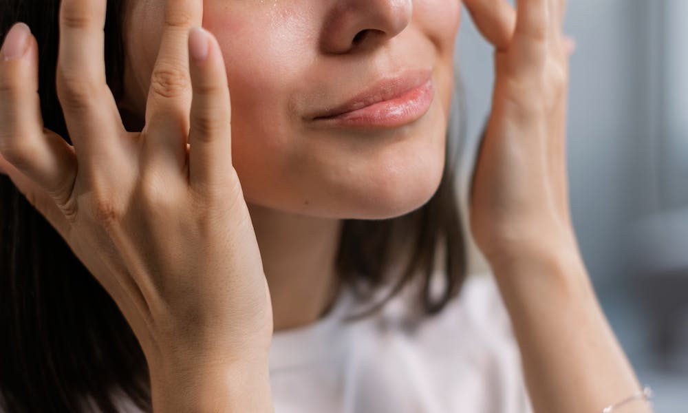 Young woman applying skincare cream with a smile, highlighting self-care and beauty routines. .pexels