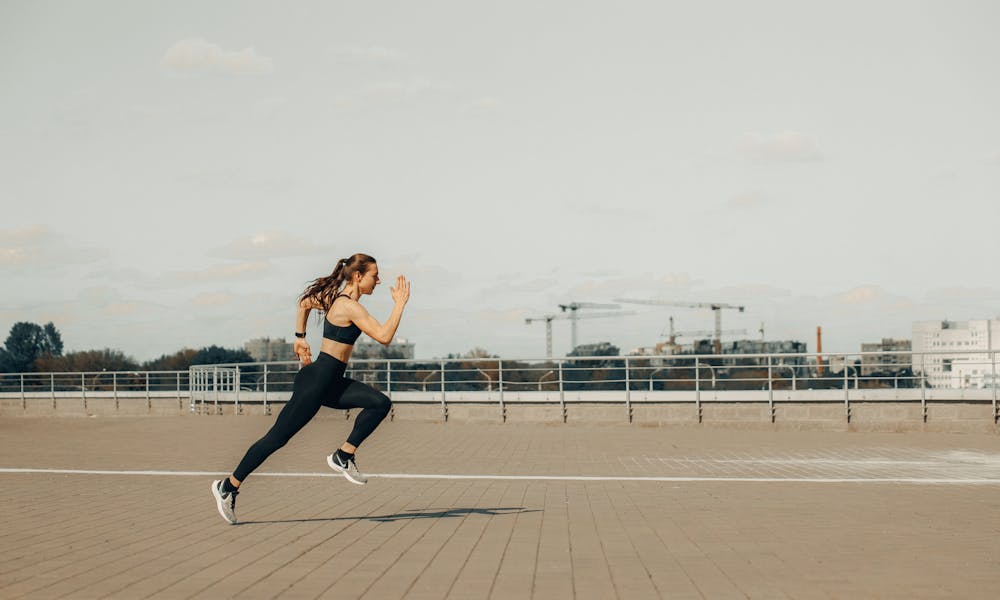 Woman sprinting on a rooftop in athletic wear during the day. .pexels