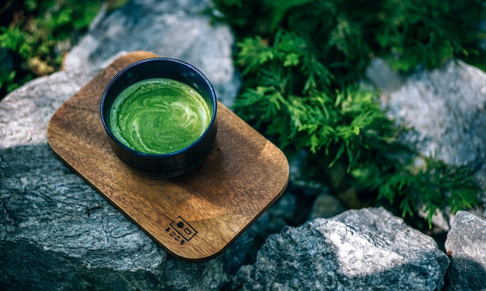 Top view of a green matcha tea served on a wooden tray outdoors, surrounded by rocks. .pexels