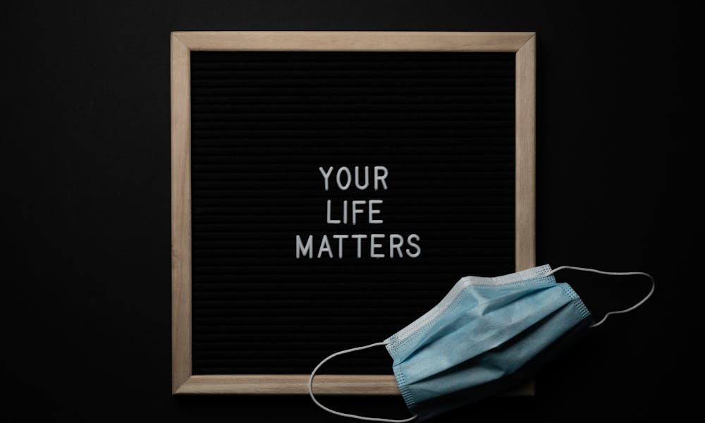 Overhead arrangement of framed black photo with white words Your Life Matters on black background near medical mask .pexels