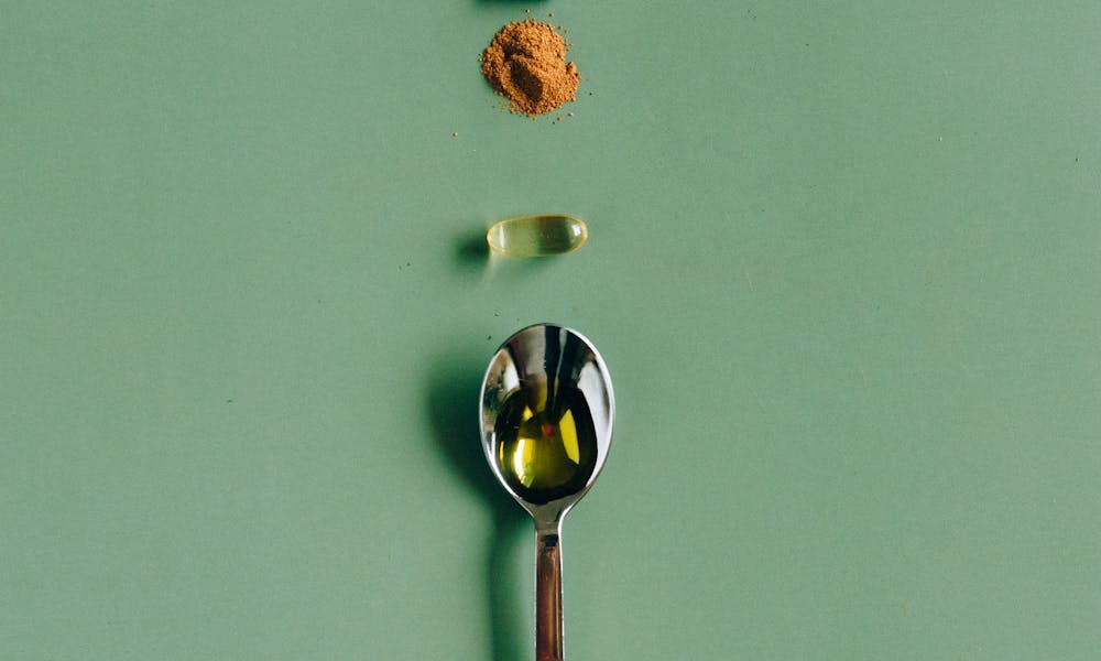 Assorted supplements and a spoon laid out on a green surface, showcasing health concepts. .pexels