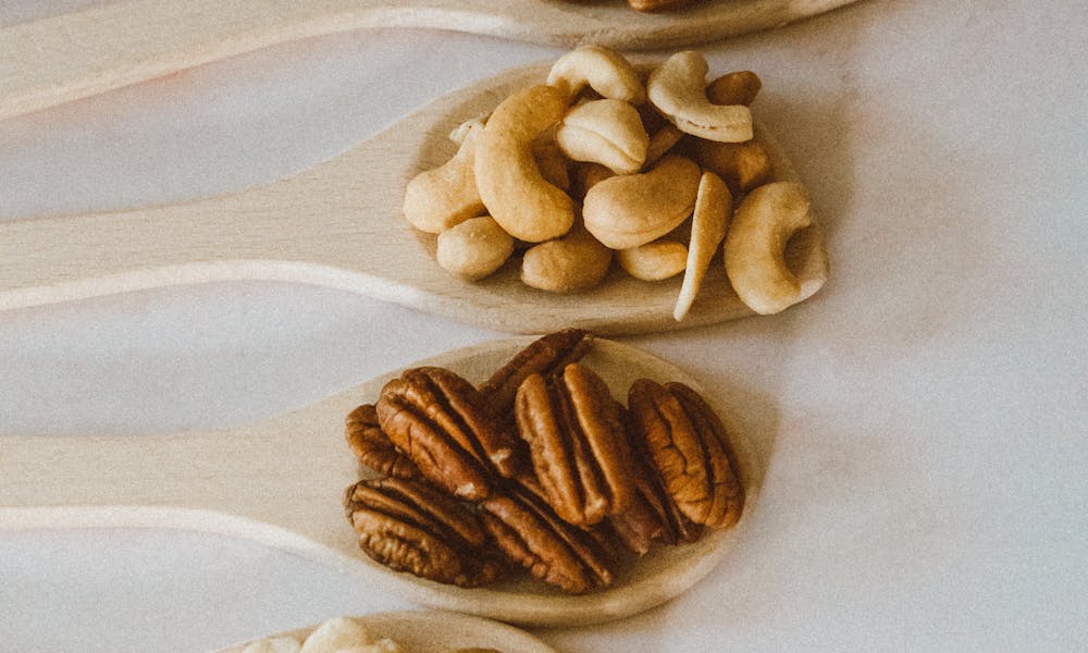 A vertical shot showcasing four types of nuts in wooden spoons, laid on a marble surface. .pexels