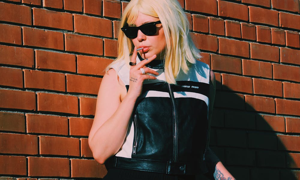 Fashionable woman in sunglasses smoking against a vibrant brick wall. .pexels