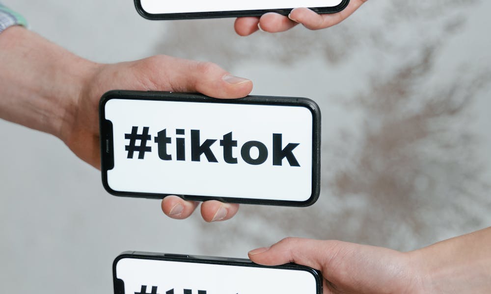 Hands holding smartphones displaying TikTok hashtag, emphasizing social media connection. .pexels