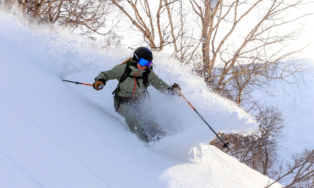 A skier navigates fresh powder on a snowy slope with bare trees in the background. .pexels